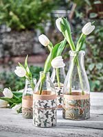 Tulips in vases of milk bottles wrapped with decorative papers.
