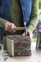 Woman hammering a nail into the bird box to keep the twig ladder in place
