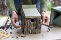 Woman wrapping wire around the birdhouse to keep the twigs in place