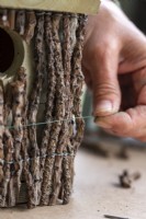 Close up of woman wrapping wire around the birdhouse to keep the twigs in place