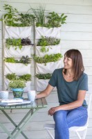 Woman sitting at a table next to hanging herb and salad garden