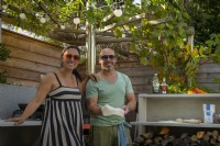 Garden owners making pizza in outdoor kitchen under pergola overgrown with Vitis - Grape Vine