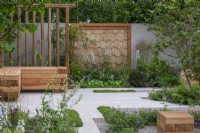The Communication Garden. A tranquil refuge with woodland planting and native wayfaring and hazel trees. The flooring is laid in planking and gravel. Wooden screens and cubes are made from sweet chestnut.