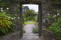 View through wall entrance in Upper Walled Garden  to formal topiary area with topiary beyond - Designer: Penelope Hobhouse - June