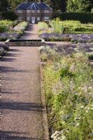 Straight gravel path leading towards the gardener's cottage at Gordon Castle Walled Garden, Scotland in July with flower beds on either side.
