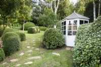 Small summerhouse framed by clipped Eleagnus x ebbingei in a garden made largely of green plants including clipped Lonicera nitida at Dip-on-the-Hill, Ousden, Suffolk in August