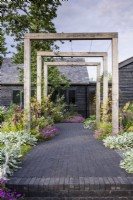 A path of Lucca brick pavers by Chelmer Valley lead beneath a simple timber pergola in July