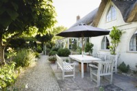 Dining area under umbrella in July outside a thatched cottage.