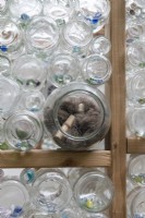 Nesting materials for birds are tucked into outward facing glass jars in recycled greenhouse walls