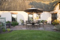 Stone patio with seating area outside thatched cottage