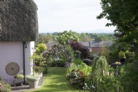 View over garden, with Clematis arch, and thatched cottage overlooking surrounding houses and countryside in early June. 