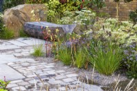 The M and G Garden. Paved area with rustic carved bench and a mix of gravel and paving for improved drainage. Autumn planting combination including  Pennisetum alopecuroides 'Cassian', Eurybia x herveyii, Sporobolus heterolepis, and Selinum wallichianum.