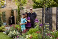 Couple with son standing near flower beds in a suburban garden