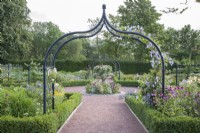 Looking through 'Gothic' arch planted with Clematis Blekitny Aniol syn. Clematis Blue Angel and scented Rosa 'Hardwell' to planter at central meeting-point of paths in contemporary walled-garden at Dumfries House. 

Lilium regale and Echinacea syn. cone-flower growing at base of arch.  Paths edged with Buxus sempervirens syn. Box. Summer, September.