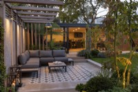 Modern garden patio and pergola at night with lighting, looking towards garden room or office