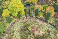 Formal columns of clipped Yew surround a semi-circular bed of grasses and perennials with several Magnolia stellata trees with autumn colour; image taken with drone. November. Autumn.