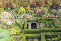 View over mature clipped hedges of Yew defining several garden rooms. Woodland at the edge of the garden. Image taken with drone. November. Autumn.