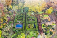 View over mature hedges of clipped Yew defining several garden rooms. Wave form hedge of Beech on right with large area planted with several different ornamental grasses in blocks; image taken with drone. November. Autumn.