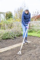 Woman using a hoe to pull weeds up from plant bed