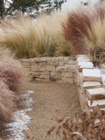 Frosty grasses planted above a stone wall that edges a path