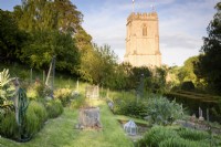 Formal vegetable garden on sloping ground at the Old Rectory, Netherbury, Dorset in May with a backdrop of St Mary's Church