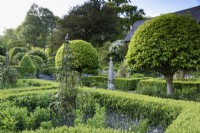 Formal garden with box hedges, clipped Portuguese laurels, Prunus lusitanica, and stone and metal obelisks at the Old Rectory, Netherbury, Dorset in May