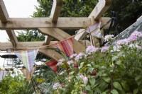  Detail of wooden arch used to hang bunting, a lamp and fitted with a bracket to support a planted hanging basket. Coombe Cottage garden. An NGS garden. July. Summer. 