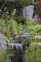 Bodmin Jail: 60 Degrees East - A Garden Between Continents. Designers: Ekaterina Zasukhina and Carly Kershaw. Waterfall, rocks and naturalistic planting. Chelsea Flower Show 2021.