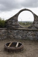 All the materials for the arch window and the fire pit have been reused and repurposed from various sources such as the local dump and from local builders. View through window to countryside. Derrydown. July. Summer. 