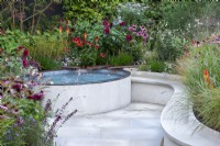 A sunken sanctuary garden where water runs along rills into a pool. Raised beds are filled with ornamental grasses, red hot pokers, coneflowers, rudbeckias and dahlias.
