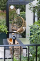 A balcony garden created as a city escape from the busy world around. An egg chair hangs from a pergola, amidst huge planters filled with foliage and flowers.