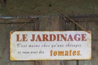 French language Le Jardinage sign hung on a door with proverb that reads gardening costs less than a therapy and you have tomatoes, Quebec, Canada