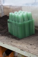 A bulk load of green plastic seed trays sit on a potting bench beside a pile of compost in a small commercial nursery. 