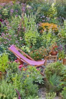 Deckchair on small patio amongst colourful mixed border and containers.