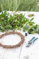 Wreath, secateurs, wire, Viburnum tinus and Portuguese laurel laid out on a wooden surface