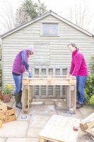 Woman drilling a pilot hole in the pallet while another woman holds it steady