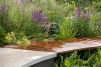 Planting next to a curved wooden walkway, including Salvia 'Amethyst'.  The Cancer Research Legacy Garden, RHS Hampton Court Palace Garden Festival 2021