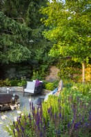 View across flower bed with Salvia nemorosa 'Caradonna' and Liquidambar to sunken seating area with lounge chairs. 