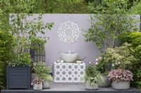 A water feature plays below a mandala, between containers planted with birch trees, acers, roses, heucheras, pelargoniums, roses and ornamental grasses. Designer: Nikki Hollier.