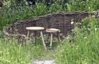Woven willow enclave in wild garden with wooden stool seats