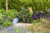 Green, purple, bronze and blue planting including Sambucus  'Black Beauty' Nepeta 'Summer Magic' and carex grasses  with wooden sculpture of Owl - SSAFA Sanctuary Garden