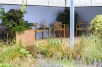 Garden with covered seating area beside a pond planted with Iris 'White Swirl' , Hostas, Carex buchananii  and Nepeta  'Summer Magic'  reflecting blue wall colour
- SSAFA Sanctuary Garden. Designer: Amanda Waring