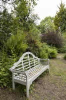 A white wooden bench underneath a variety of cottage garden style planting. Lewis Cottage, NGS Devon garden. Spring.