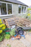 Pallets, compost, compost scoop, watering can, lining, scissors, tiles, screws, screwdriver, pencil, tape measure, drill, basin, twigs, logs and various dried plants laid out on the ground