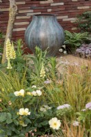 A bronze urn in a contemporary patio garden, with a golden themed border containing Anemanthele lessoniana, Rosa 'Tottering by Gently' and Pimpinella major 'Rosea'