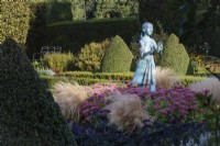The Formal Garden, with a knot garden of Buxus sempervirens,  Box and Berberis hedging. The statue of a young girl stands amongst Sedum 'Autumn Joy', Sedums, Heliotropium arborescens, Heliotrope, and  Stipa tenuissima, Mexican Feather Grass.  Waterperry Gardens, Wheatley, Oxfordshire, UK