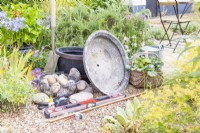 Shallow container, faux barrel container, cobbles, water pump, glue, spirit level, copper pipe, pipe cutter, pencil, spade, watering can and plants laid out on the ground