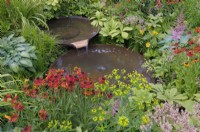 Water flowing between two staggered Torc Pots corten steel water bowls surrounded with colourful plants including helenium, euphorbia and astilbe.  The Daily Mail and RHS Planet-Friendly Garden, RHS Hampton Court Palace Garden Festival 2022.  Designer: Mark Gregory 