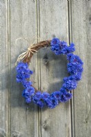 Rustic wreath decorated with flowers of Centurea cyanus against wooden background