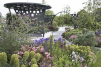 Metal pergola and moongate amongst colourful planting in the CRUK Legacy Garden at RHS Malvern Spring Festival 2022